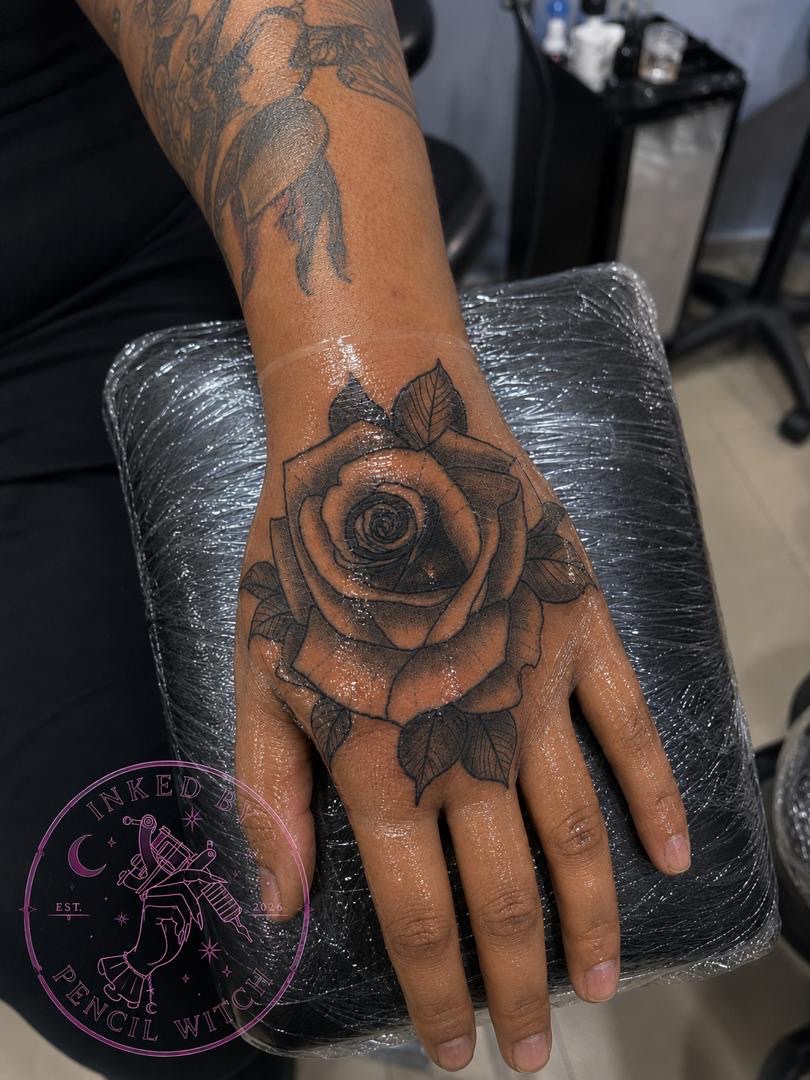 Detailed black and grey rose tattoo on the back of a hand