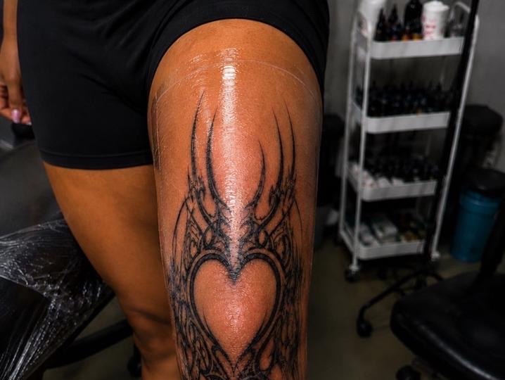 Intricate ornamental black-and-grey tattoo on the knee with a heart at center